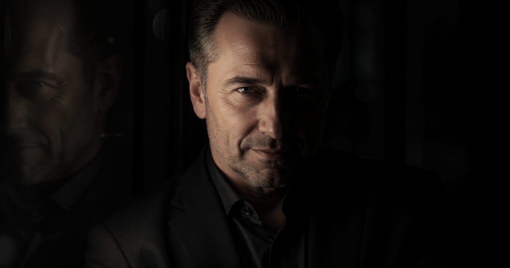 Portrait illustrating malignant narcissist manipulation tactics, with one side of the man’s face lit and the other concealed in shadow.
